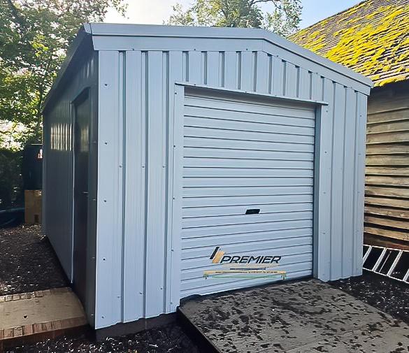 Front view of a light blue or grey steel shed featuring a single roller door and a side entrance door.
